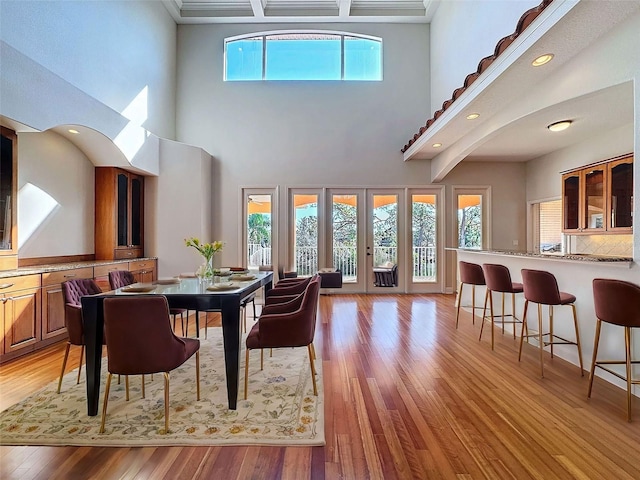 dining area featuring light wood-type flooring, a towering ceiling, and french doors