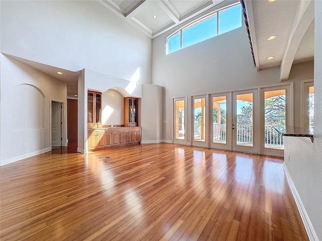 unfurnished living room featuring french doors, baseboards, beamed ceiling, and light wood-style flooring