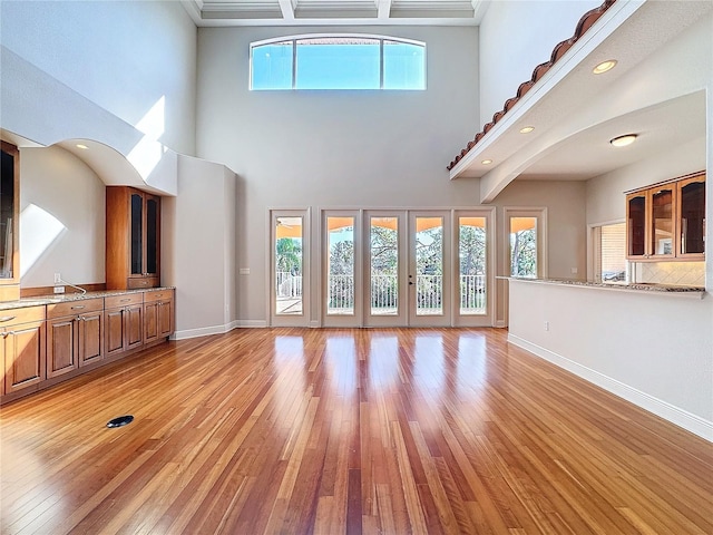 unfurnished living room featuring a high ceiling, french doors, light wood-style floors, and baseboards