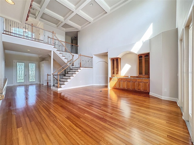 unfurnished living room featuring stairway, baseboards, coffered ceiling, light wood-style flooring, and french doors