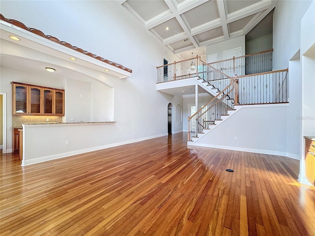 unfurnished living room featuring coffered ceiling, stairway, arched walkways, light wood finished floors, and baseboards