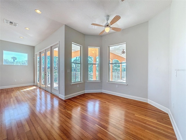 unfurnished room with hardwood / wood-style floors, baseboards, visible vents, and a textured ceiling