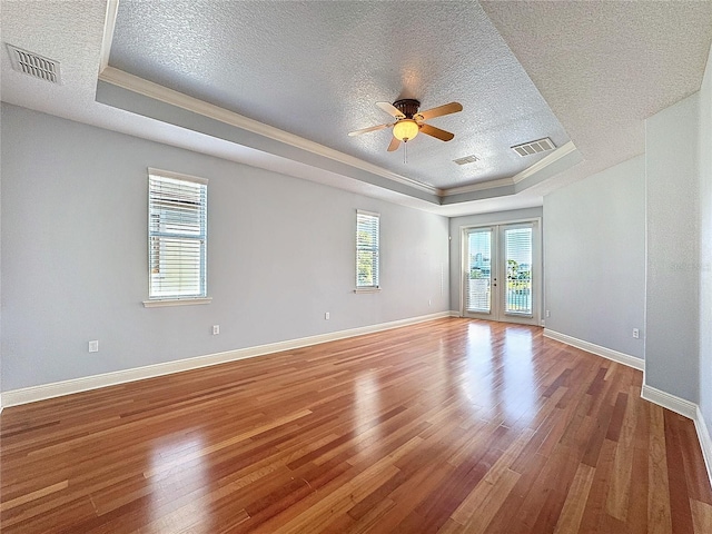 empty room with visible vents, a raised ceiling, and wood finished floors