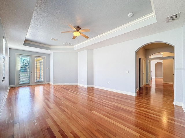 unfurnished living room featuring visible vents, a tray ceiling, arched walkways, light wood-style floors, and a textured ceiling