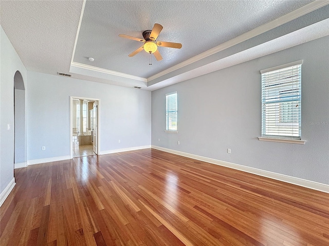 unfurnished room featuring a tray ceiling, arched walkways, visible vents, and wood finished floors