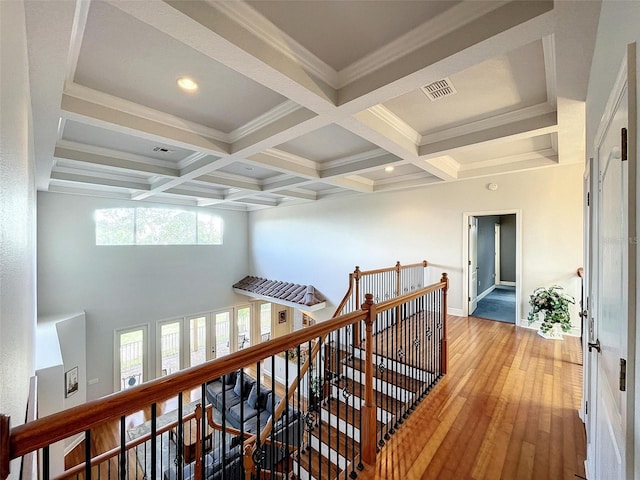 hall featuring an upstairs landing, beam ceiling, coffered ceiling, and light wood-style floors