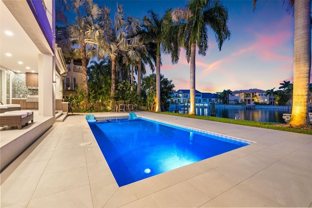 pool at dusk featuring a water view, a patio area, and an outdoor pool