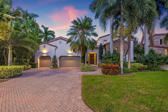 mediterranean / spanish house featuring a garage, a yard, decorative driveway, and stucco siding