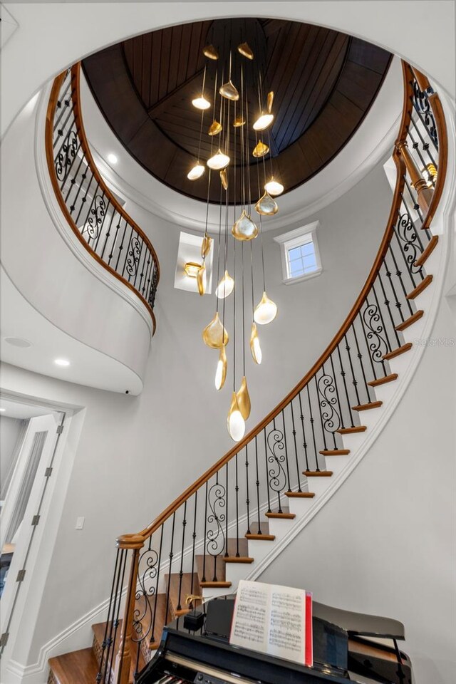 staircase with a chandelier, a raised ceiling, baseboards, and a high ceiling