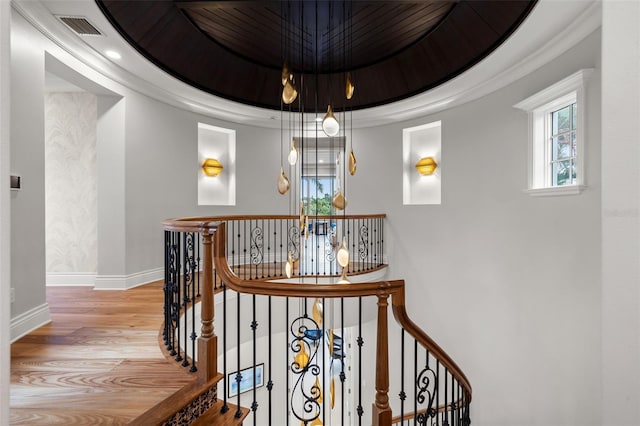 staircase with a tray ceiling, wood finished floors, visible vents, and baseboards