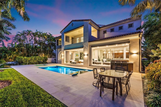 rear view of house featuring a fenced in pool, a patio, stucco siding, a balcony, and an outdoor bar