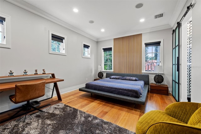 bedroom with ornamental molding, a barn door, wood finished floors, and visible vents