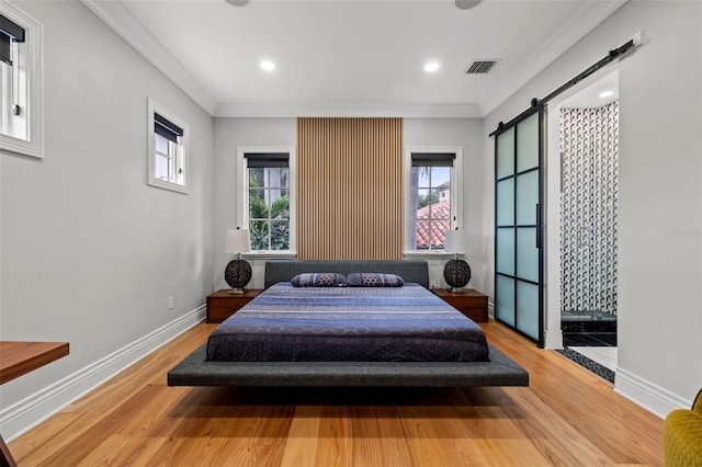 bedroom featuring a barn door, wood finished floors, visible vents, and crown molding