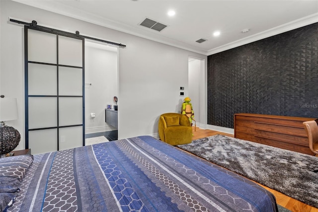 bedroom featuring visible vents, a barn door, ornamental molding, an accent wall, and baseboards