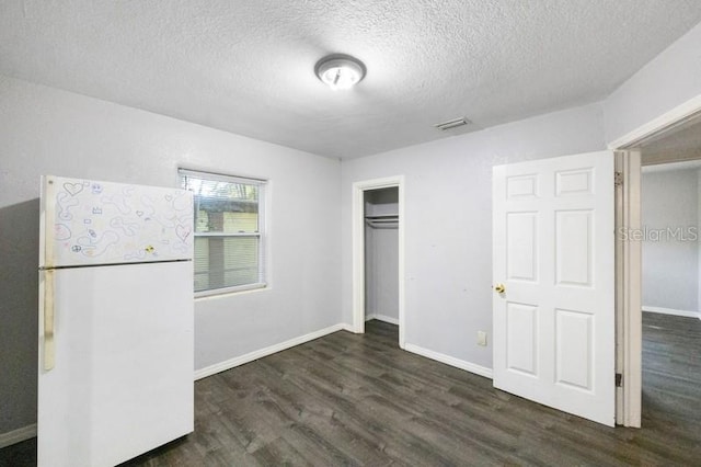 unfurnished bedroom featuring a closet, dark hardwood / wood-style floors, white refrigerator, and a textured ceiling