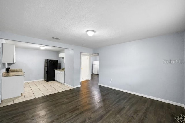 kitchen with light hardwood / wood-style floors, white cabinets, black fridge, and washer / clothes dryer