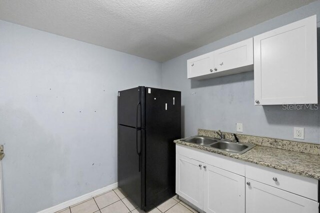 kitchen with black fridge, light tile patterned flooring, sink, a textured ceiling, and white cabinets