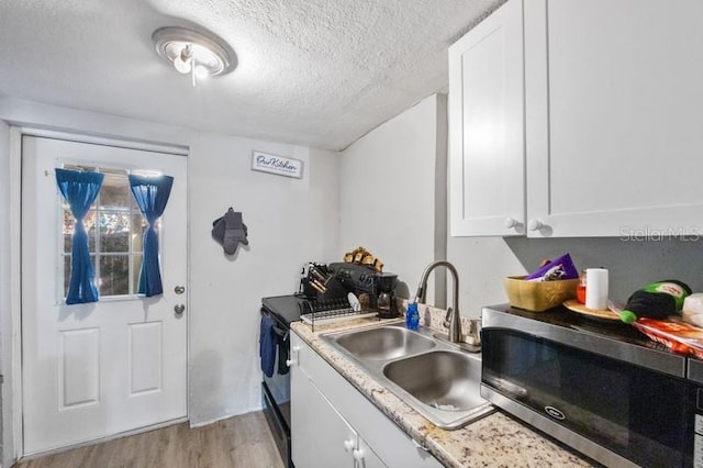 kitchen with white cabinets, light wood-type flooring, sink, and a textured ceiling