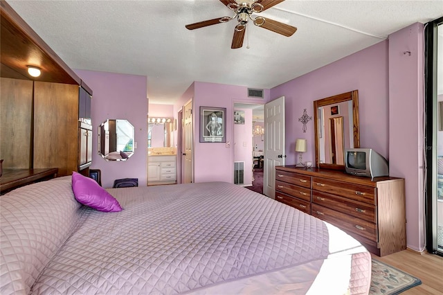 bedroom with a textured ceiling, ensuite bathroom, light hardwood / wood-style flooring, and ceiling fan