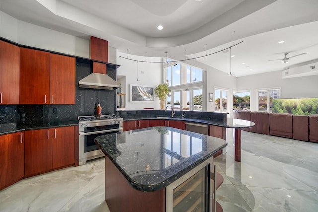 kitchen with wall chimney range hood, ceiling fan, appliances with stainless steel finishes, wine cooler, and dark stone countertops