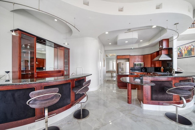 kitchen featuring appliances with stainless steel finishes, wall chimney exhaust hood, a raised ceiling, light tile patterned floors, and kitchen peninsula