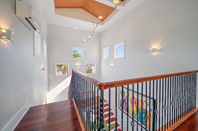 hallway with hardwood / wood-style flooring, a towering ceiling, and a wall unit AC