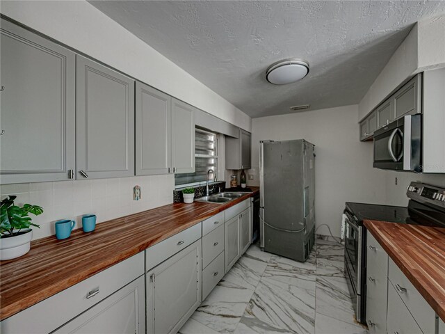 kitchen featuring wooden counters, appliances with stainless steel finishes, decorative backsplash, sink, and gray cabinets