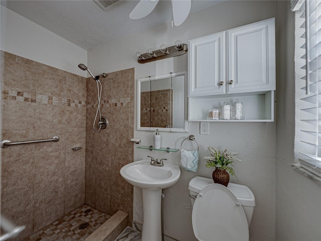 bathroom with a tile shower, a textured ceiling, ceiling fan, sink, and toilet