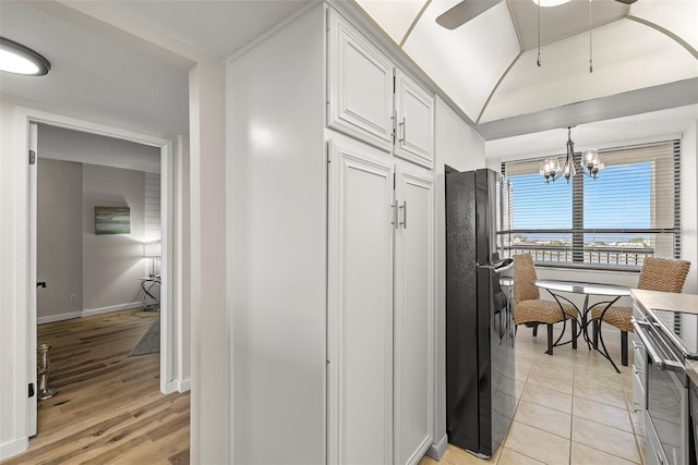 kitchen with light tile patterned flooring, ceiling fan with notable chandelier, white cabinetry, stainless steel electric range, and freestanding refrigerator