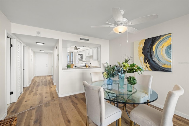 dining room with light wood-style floors, visible vents, baseboards, and a ceiling fan