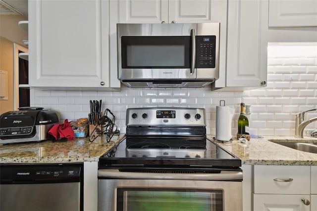 kitchen featuring sink, white cabinets, backsplash, stainless steel appliances, and light stone countertops