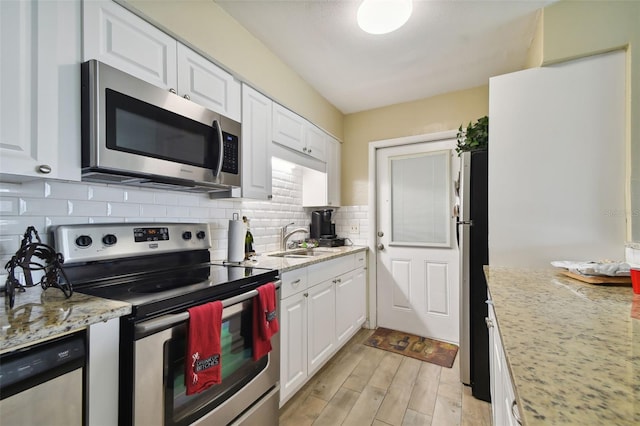 kitchen with stainless steel appliances, white cabinetry, sink, and light stone counters