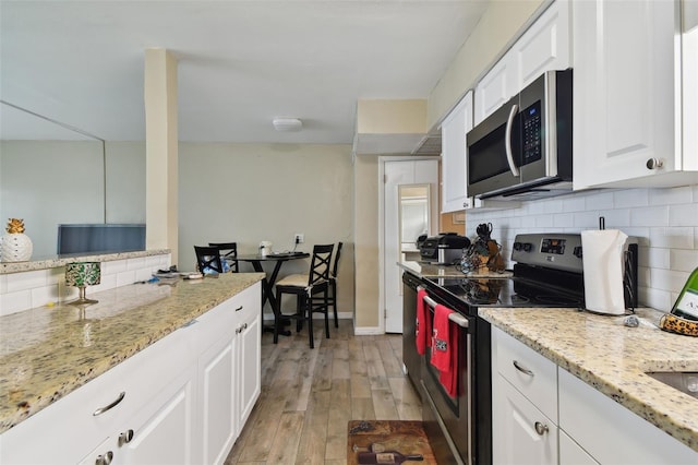 kitchen with appliances with stainless steel finishes, white cabinetry, decorative backsplash, light stone counters, and light hardwood / wood-style floors