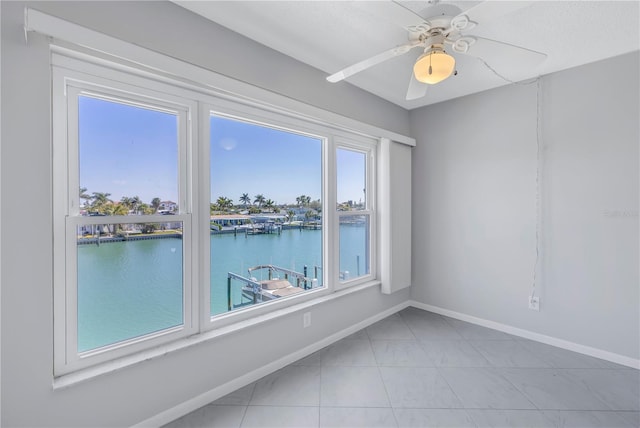 tiled spare room featuring plenty of natural light, ceiling fan, and a water view