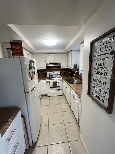 kitchen featuring dark countertops, white cabinets, a sink, white appliances, and under cabinet range hood
