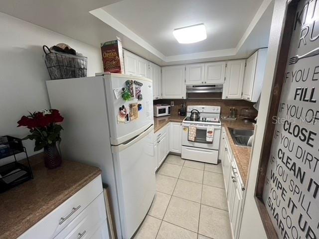 kitchen with white appliances, white cabinets, dark countertops, under cabinet range hood, and light tile patterned flooring