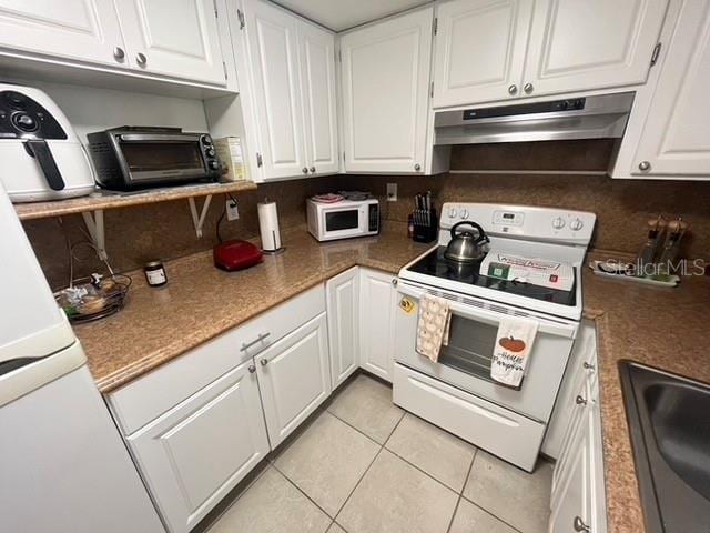 kitchen with light tile patterned floors, under cabinet range hood, white appliances, a sink, and white cabinets