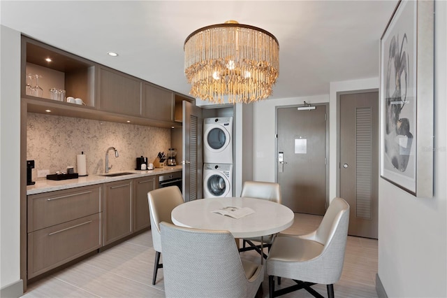 tiled dining space with a notable chandelier, stacked washer and clothes dryer, and sink