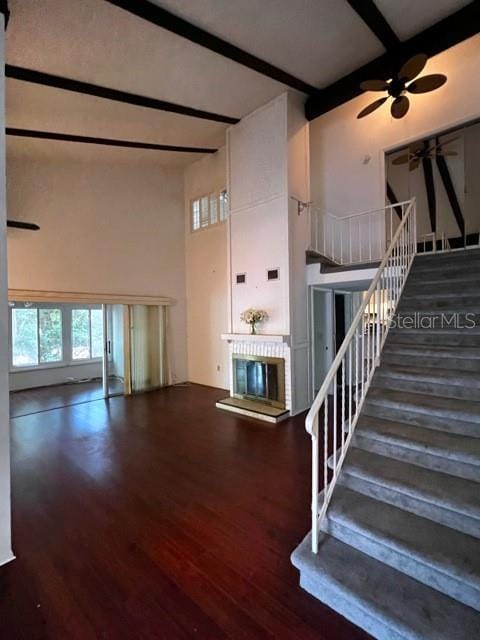 interior space featuring a brick fireplace, a towering ceiling, ceiling fan, beam ceiling, and hardwood / wood-style floors