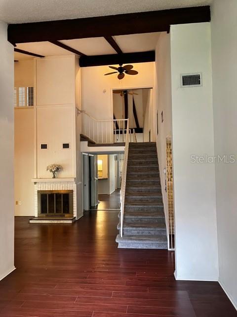 staircase featuring a towering ceiling, a fireplace, hardwood / wood-style flooring, ceiling fan, and beam ceiling