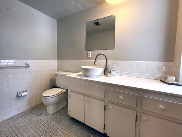 bathroom featuring tile walls, vanity, a textured ceiling, tile patterned floors, and toilet