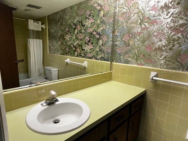 full bathroom featuring vanity, tile walls, shower / tub combo with curtain, and toilet