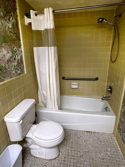 bathroom with tile walls, tile patterned floors, shower / bath combo with shower curtain, and toilet