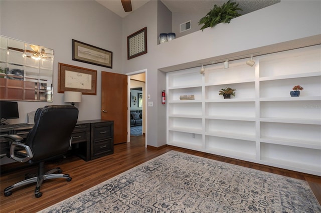 office with built in shelves, dark wood-type flooring, and high vaulted ceiling