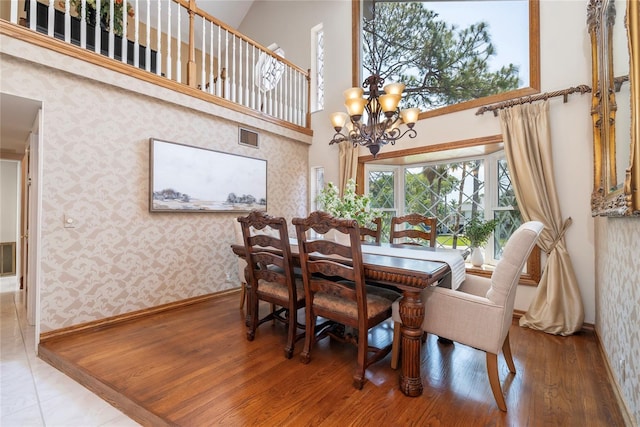 761 Soundview Dr, Palm Harbor, FL 34683 - dining area featuring wallpapered walls, baseboards, a chandelier, wood finished floors, and a towering ceiling