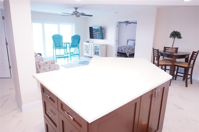 kitchen with open floor plan, light countertops, a ceiling fan, a kitchen island, and marble finish floor