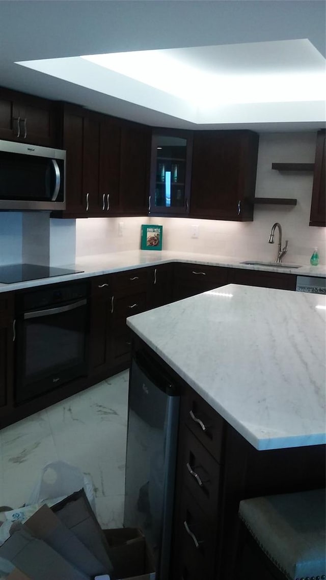 kitchen featuring dark brown cabinetry, decorative backsplash, sink, and black appliances