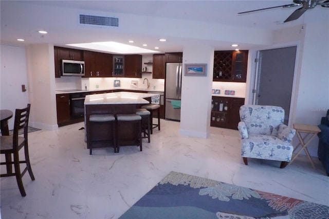 kitchen with a breakfast bar, dark brown cabinets, stainless steel appliances, sink, and a kitchen island