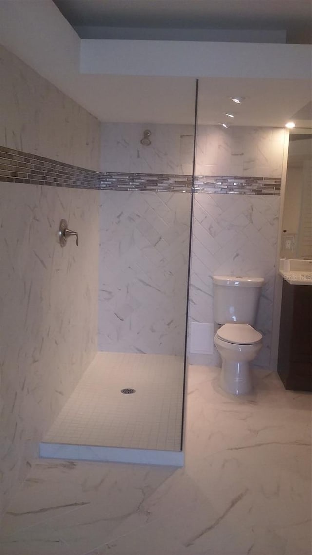 bathroom featuring tiled shower, vanity, tile walls, and toilet