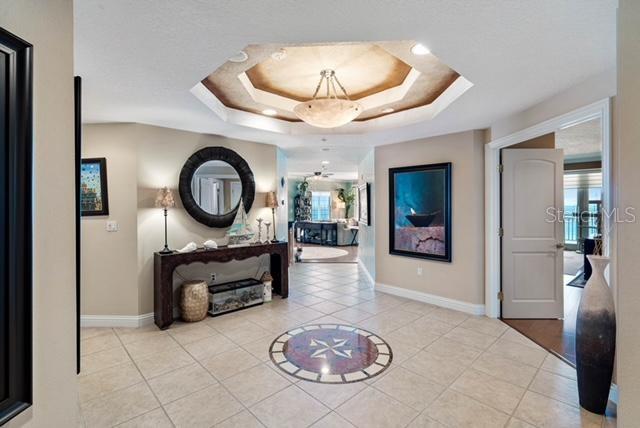 corridor with a tray ceiling and light tile patterned floors